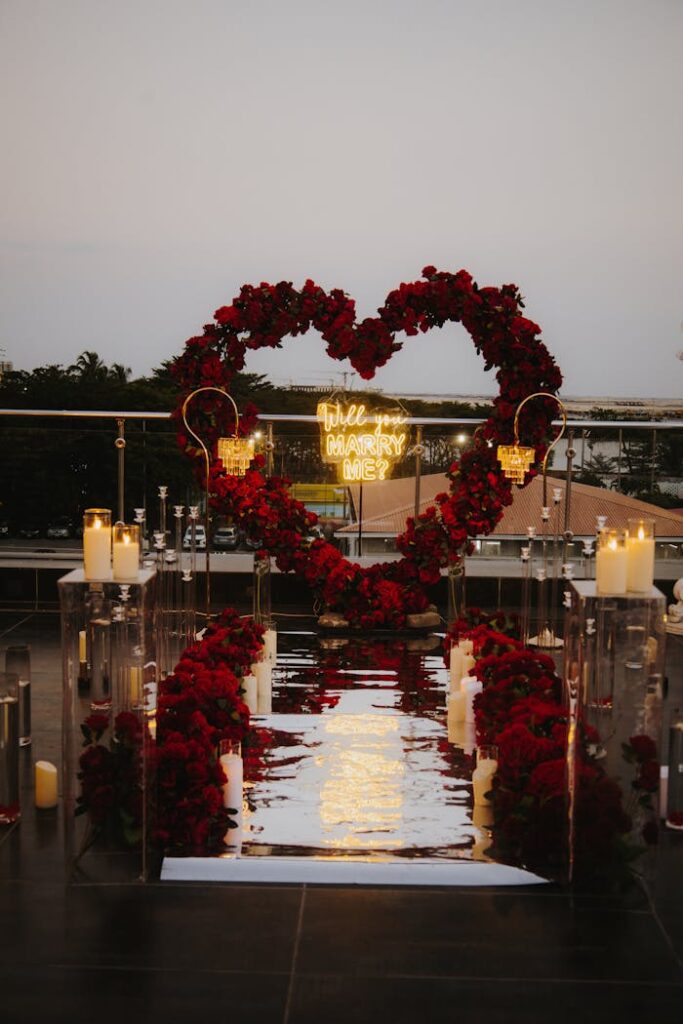 pexels-photo-29616928 A stunning rooftop proposal setup with a rose heart arch and candles at sunset.